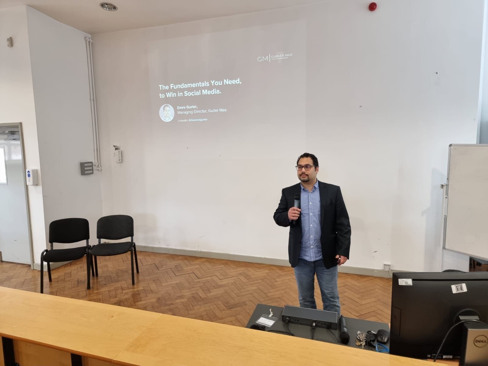 Emre, giving a presentation in front of a projector screen in a lecture hall.