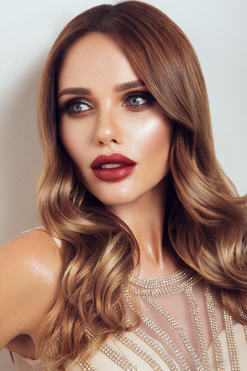 A woman with long brown hair and red lips is wearing a white dress.