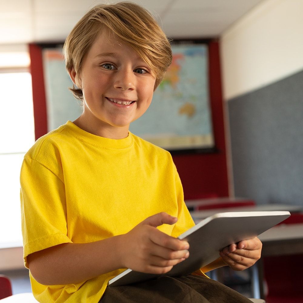 A young boy in a yellow shirt is holding a tablet