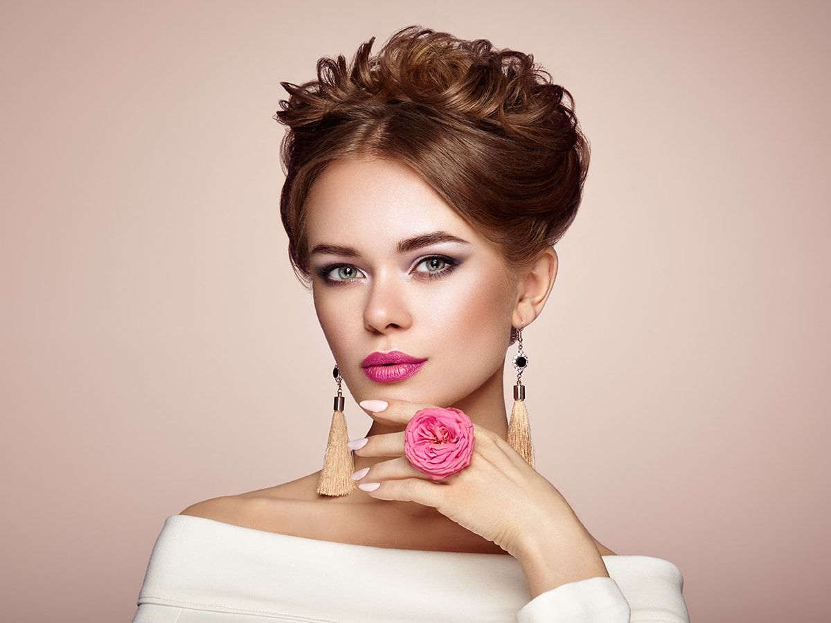 A woman wearing earrings and a ring with a pink flower on her finger.
