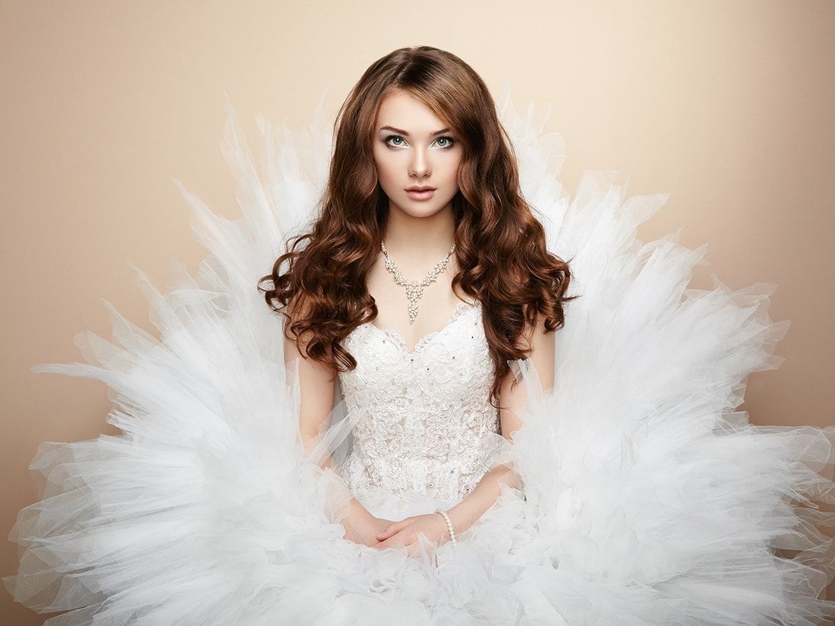 A woman in a wedding dress is sitting in front of a pile of white feathers.