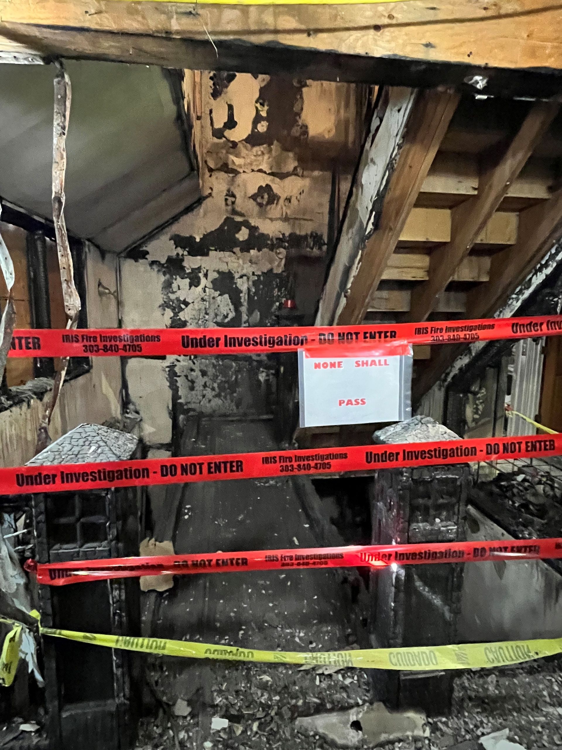 Fire-damaged interior with caution tape. Charred walls, exposed beams, and a staircase - HRS Restoration Services in Littleton, CO.