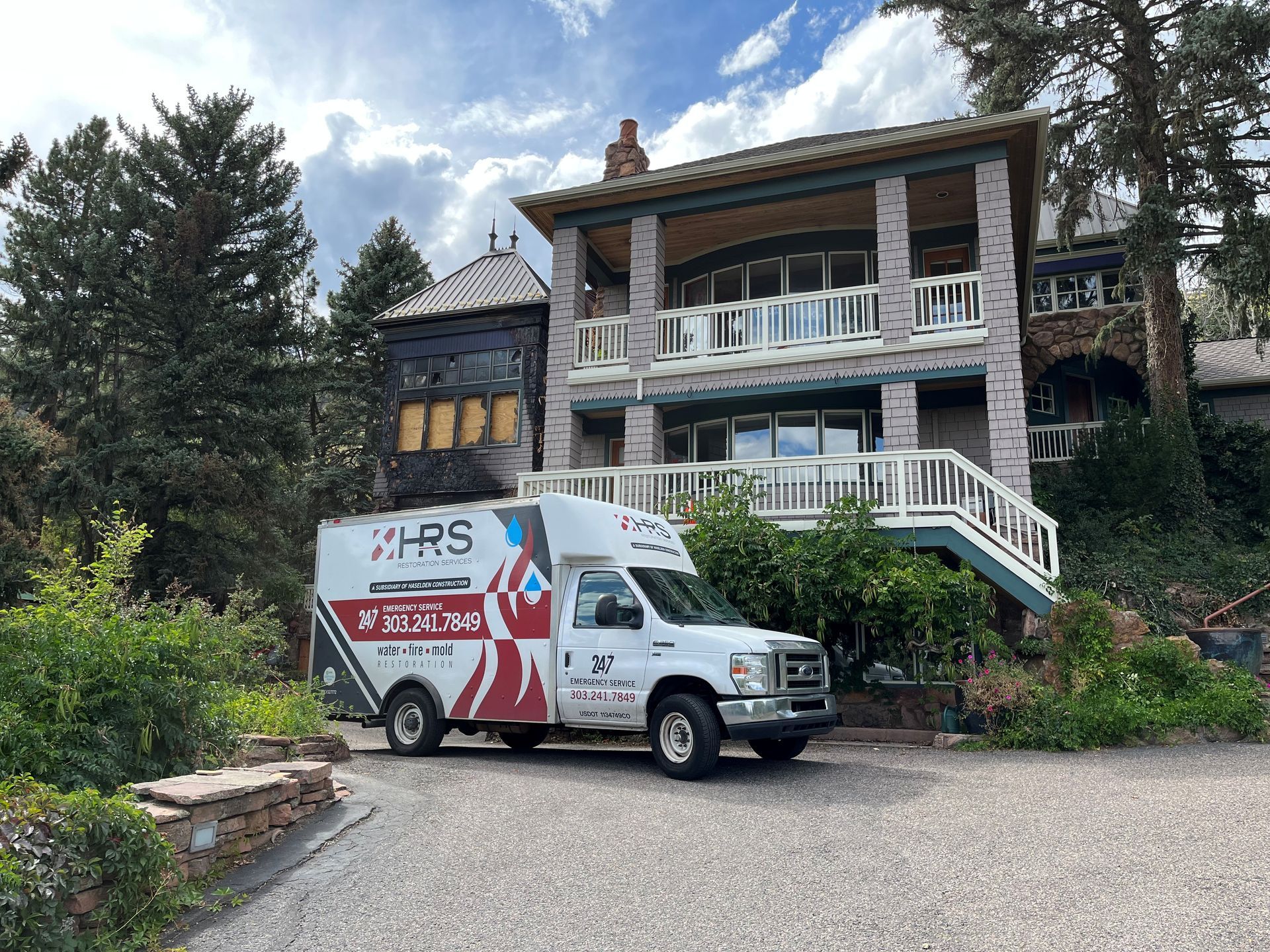 White service van parked in front of a large two-story house with a balcony and a stone exterior.