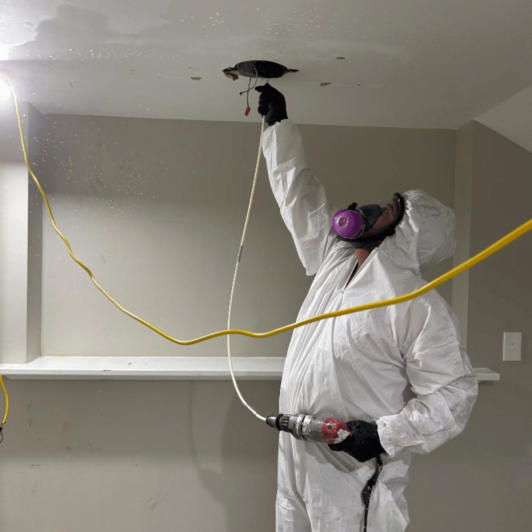 Person in protective suit drilling into a ceiling. Restoration services provided by HRS in Colorado Springs, CO.