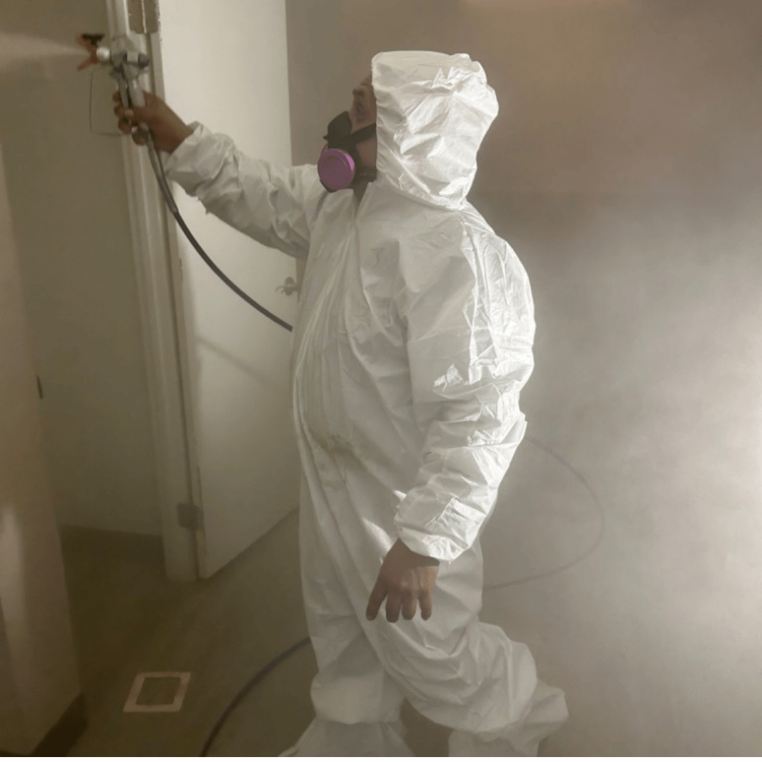 Person in white protective suit spraying a wall with a paint sprayer - HRS Restoration Services in Littleton, CO.