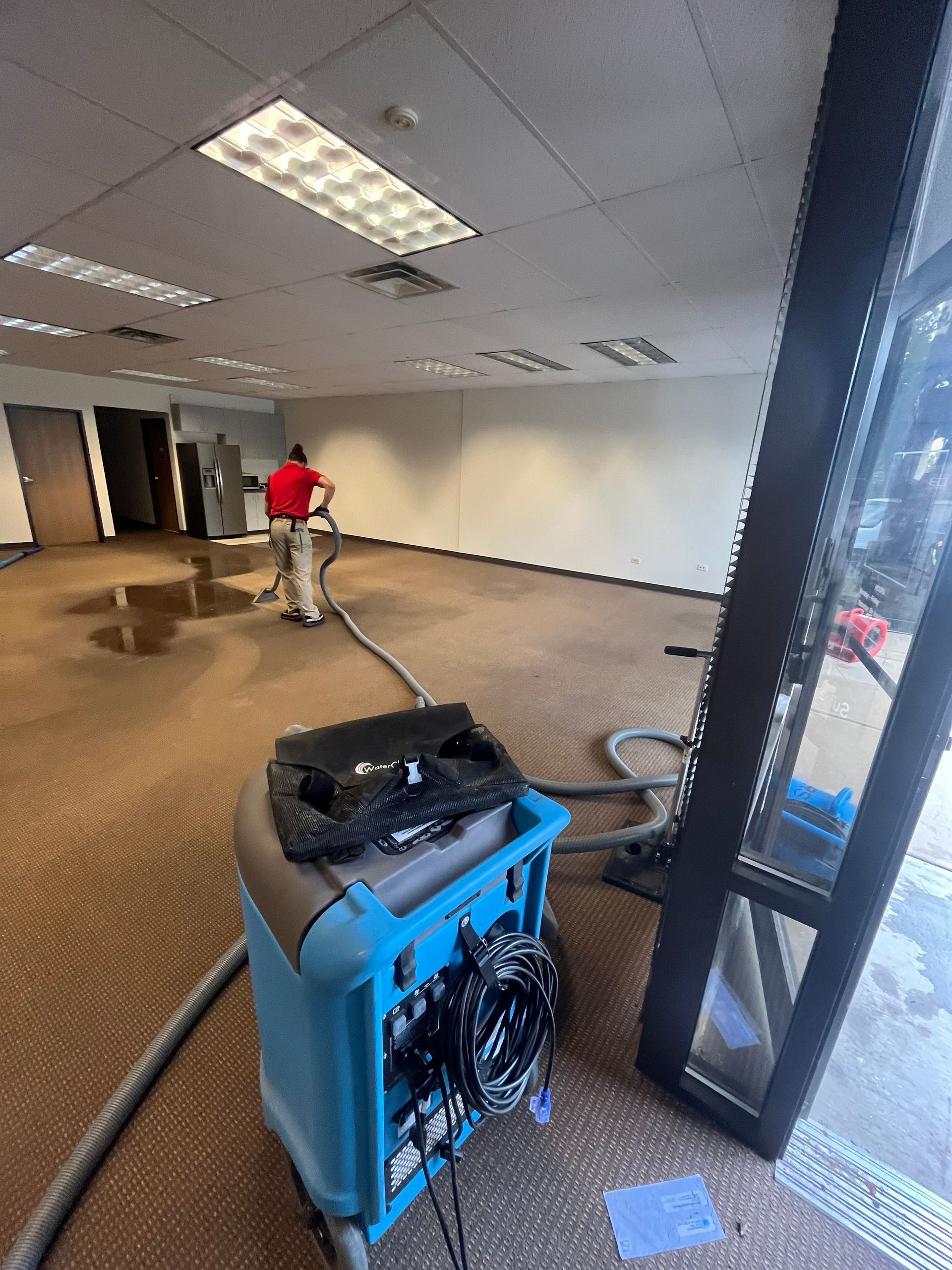 A person uses a water extraction machine to remove water from a flooded office carpet - HRS Restoration Services.