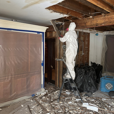 Person in protective suit on ladder removing debris from a room under renovation.