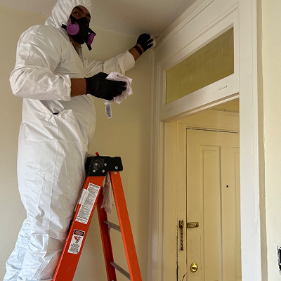 Person in a white hazmat suit on a ladder, wiping a wall. Doorway visible.