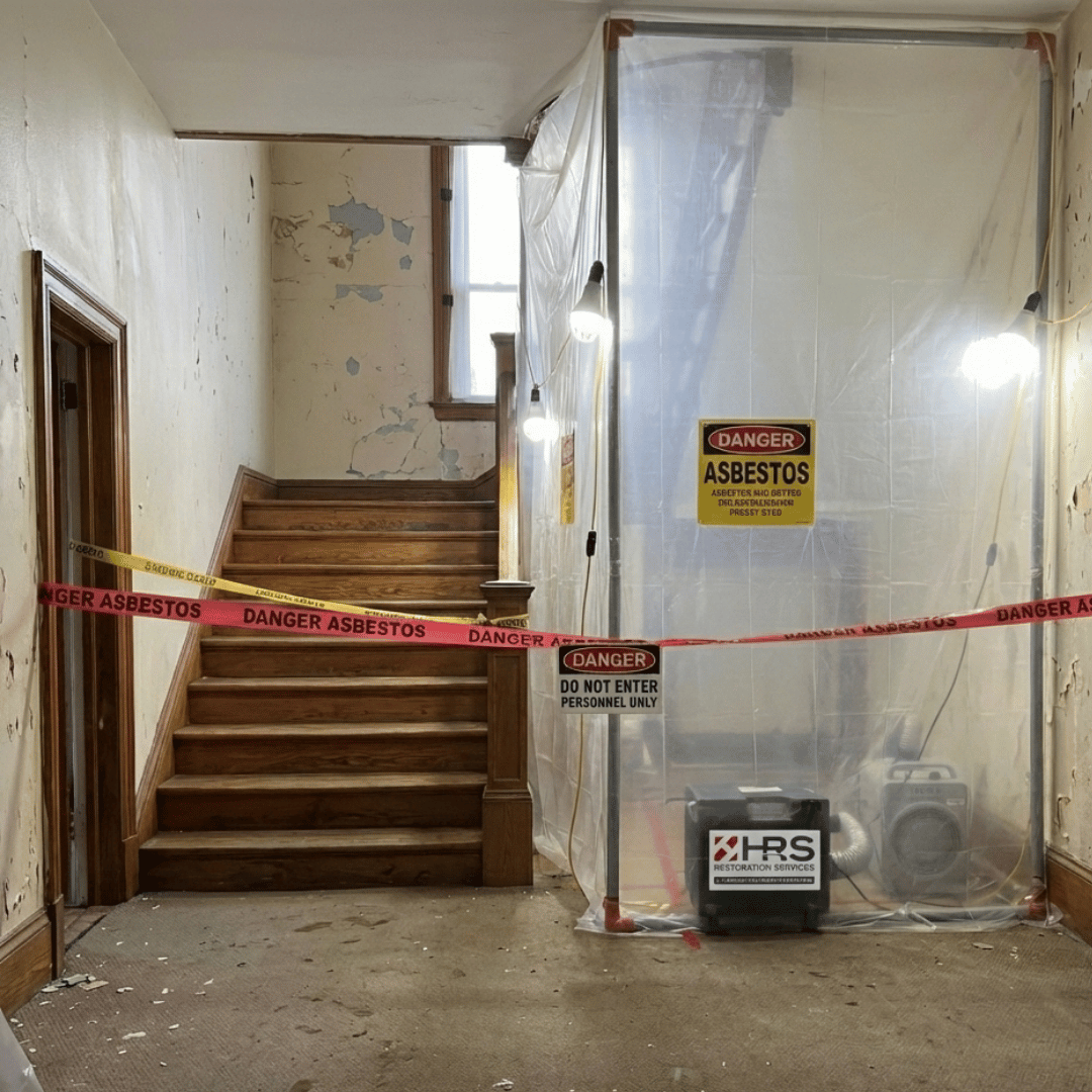 Full asbestos removal containment area in a Lakewood home using sealed barriers, warning signage, and HEPA air scrubbers by HRS Restoration Services.