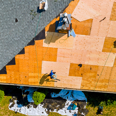 Aerial view of roof construction: workers on new wood roof, old shingles nearby.