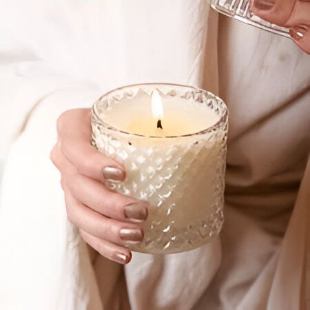 Persona sosteniendo una vela blanca encendida en un frasco de vidrio decorativo.