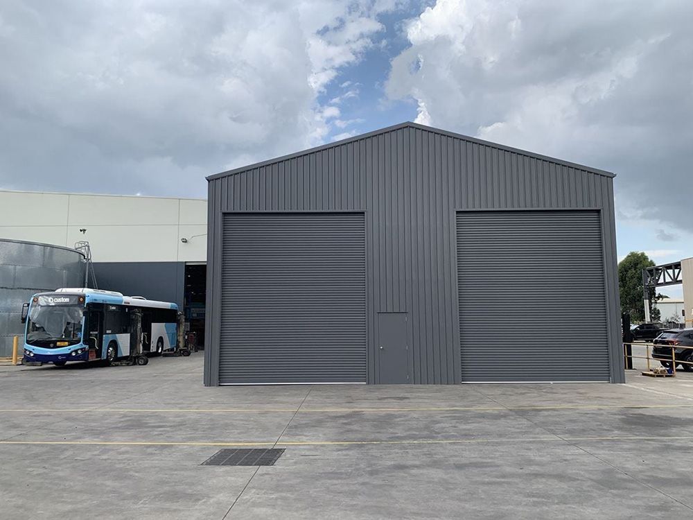 A Bus Is Parked in Front of A Large Gray Building — ShedPro Constructions in Darawank, NSW