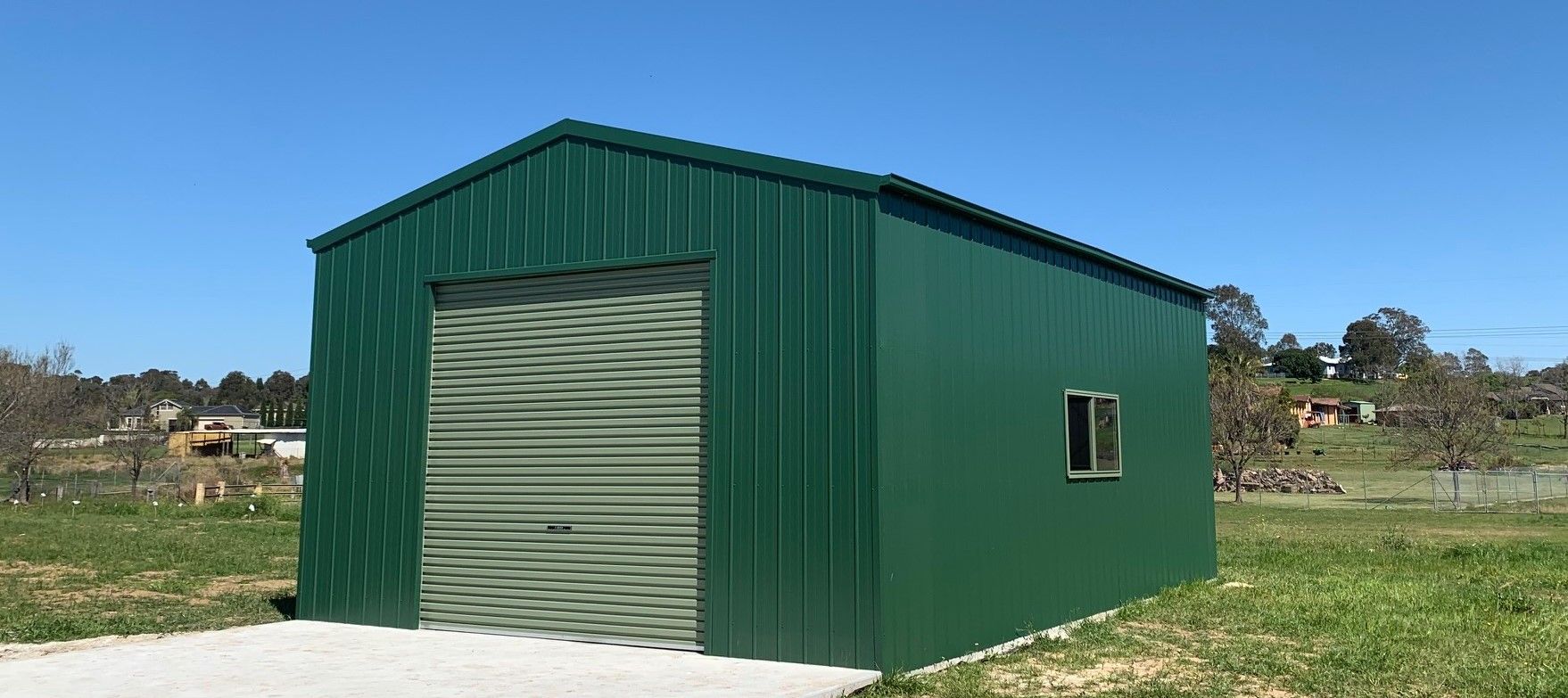 A Green Shed With a Roll Up Door and a Window — ShedPro Constructions in Taree, NSW