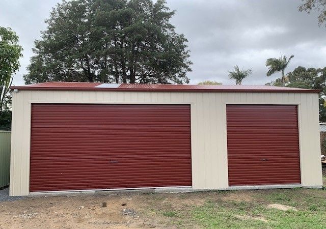 Cream Triple Garage With Red Double and Single Roller Doors — ShedPro Constructions in Kempsey, NSW
