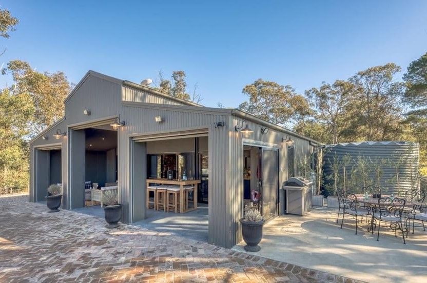 A Large House With a Patio and Tables and Chairs in Front of It — ShedPro Constructions in Wingham, NSW