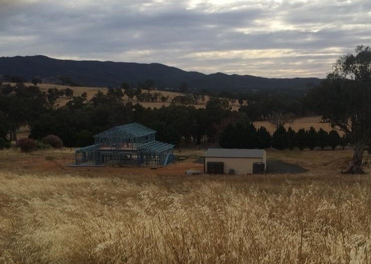 A House is Being Built in a Field With Mountains in the Background — ShedPro Constructions in Smiths Lake, NSW