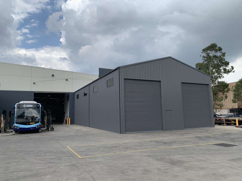 A Blue Bus Is Parked in Front of A Large Building — ShedPro Constructions in Darawank, NSW