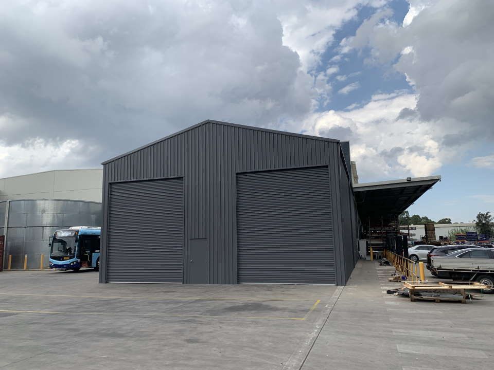 A Large Gray Building with A Bus Parked in Front of It — ShedPro Constructions in Darawank, NSW