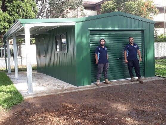 Two Men Are Standing in Front of A Green Garage — ShedPro Constructions in Darawank, NSW