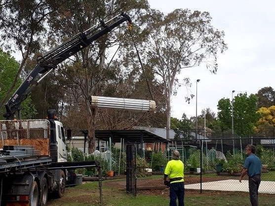 A Man in a Yellow Vest is Standing Next to a Truck With a Crane Attached to It — ShedPro Constructions in Darawank, NSW