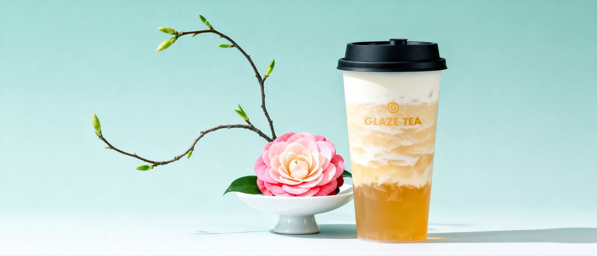 A white takeaway cup labeled "GLAZE TEA" suspended in the air, encircled by two white calla lily flowers against teal.