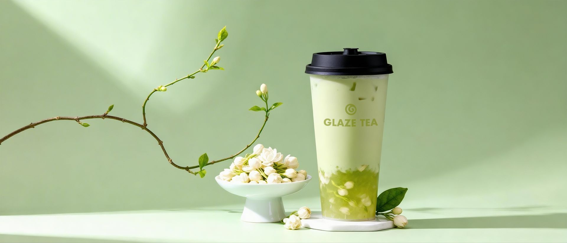 A white takeaway cup labeled "GLAZE TEA" suspended in the air, encircled by two white calla lily flowers against teal.