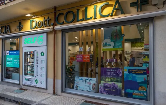 Luminoso corridoio della farmacia con scaffali bianchi pieni di medicinali, scatole e flaconi.