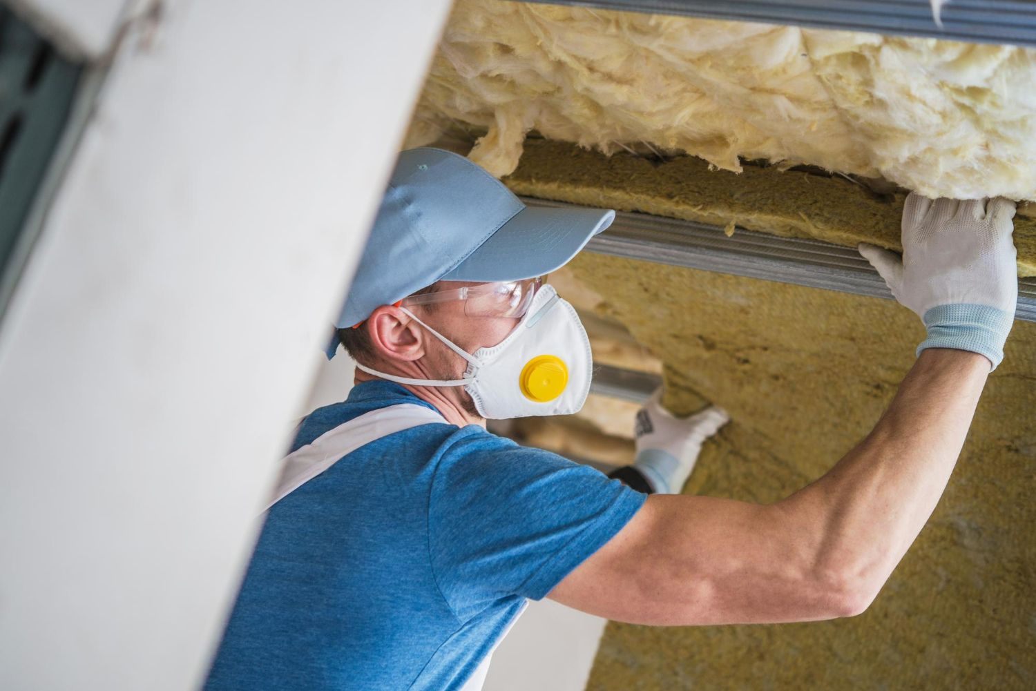 A man wearing a mask and gloves is working on a ceiling.
