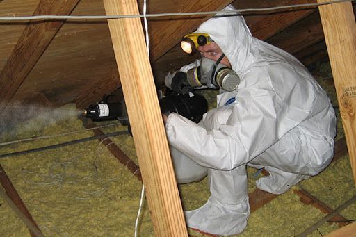 A person in a protective suit is spraying mold on a wall.