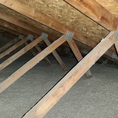 A man wearing a mask is laying a roll of insulation on the floor.