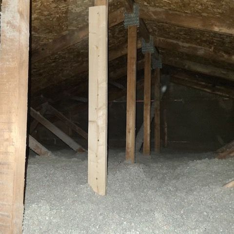 A man is blowing insulation into a pipe in an attic.