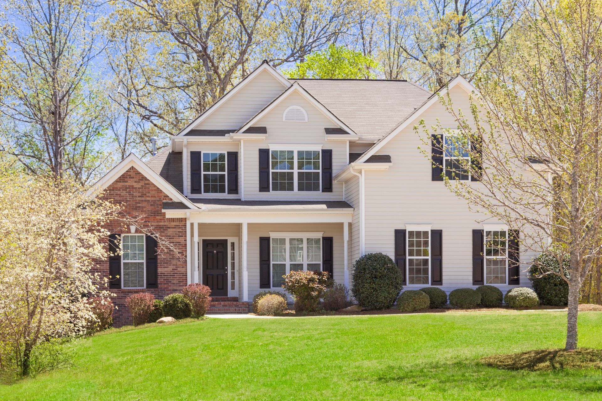 A large white house with black shutters sits on a lush green lawn