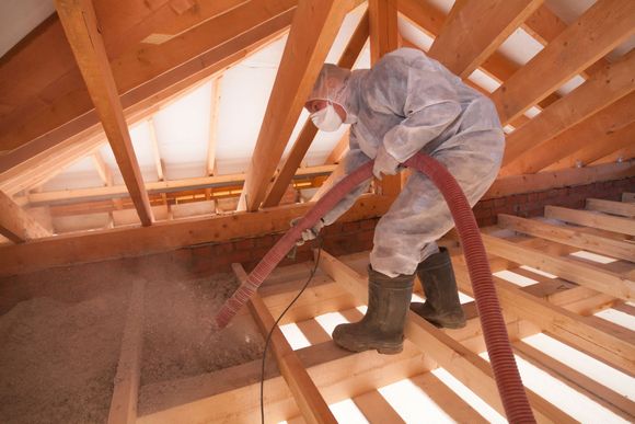 A man in a protective suit is insulating a wall in a house.