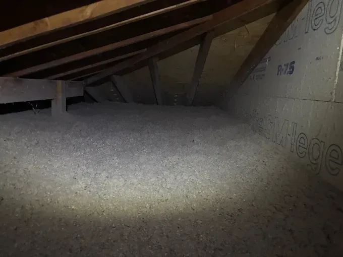 Attic insulation between wooden rafters, with a light beam illuminating the grey, textured surface.