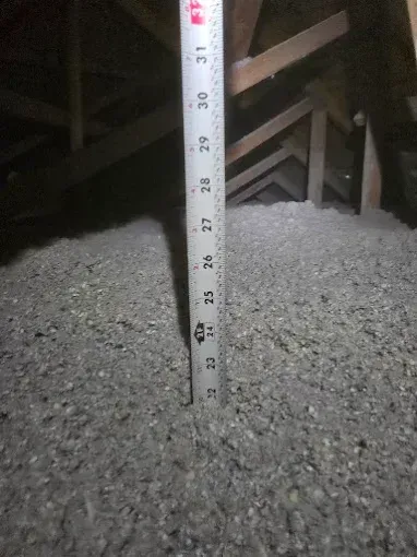 A measuring tape shows a depth of approximately 22 inches of blown-in insulation inside an attic.