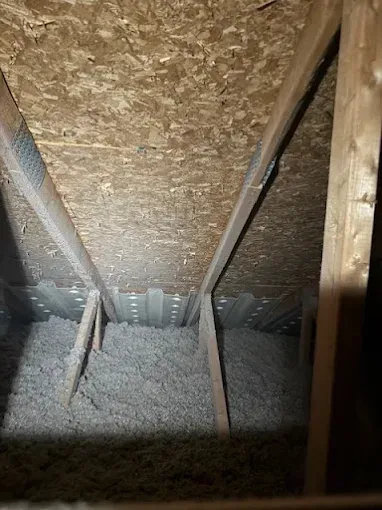 Attic interior with wooden rafters, OSB roof sheathing, and loose-fill insulation between the roof trusses.