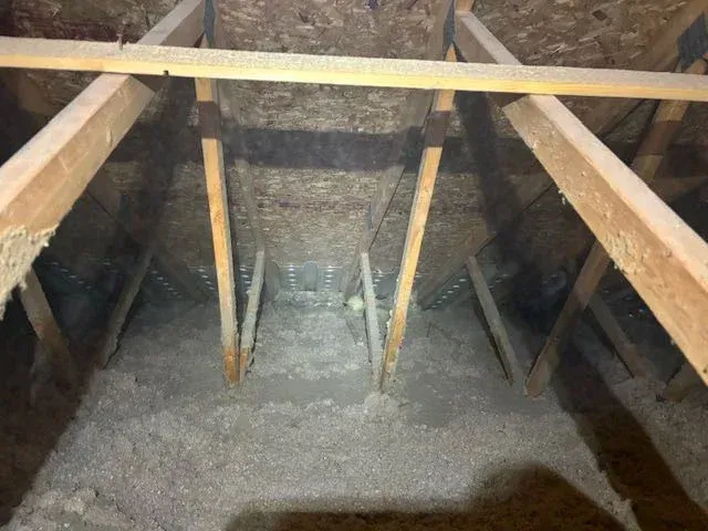 A view inside an attic showing wooden roof trusses, metal connector plates, and a layer of loose-fill insulation.