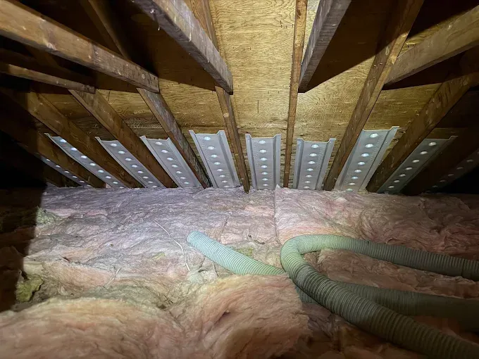 An attic showing rafter vents installed between wood roof joists above pink fiberglass insulation.
