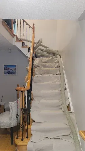 A staircase with tan protective paper covering the steps and a grey vacuum hose running up the center of the stairs.