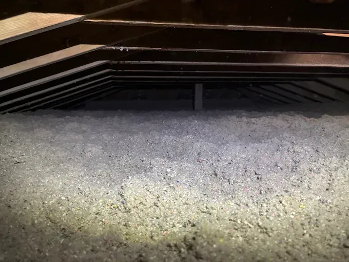 A metal soffit vent installed above a layer of grey blown-in attic insulation.