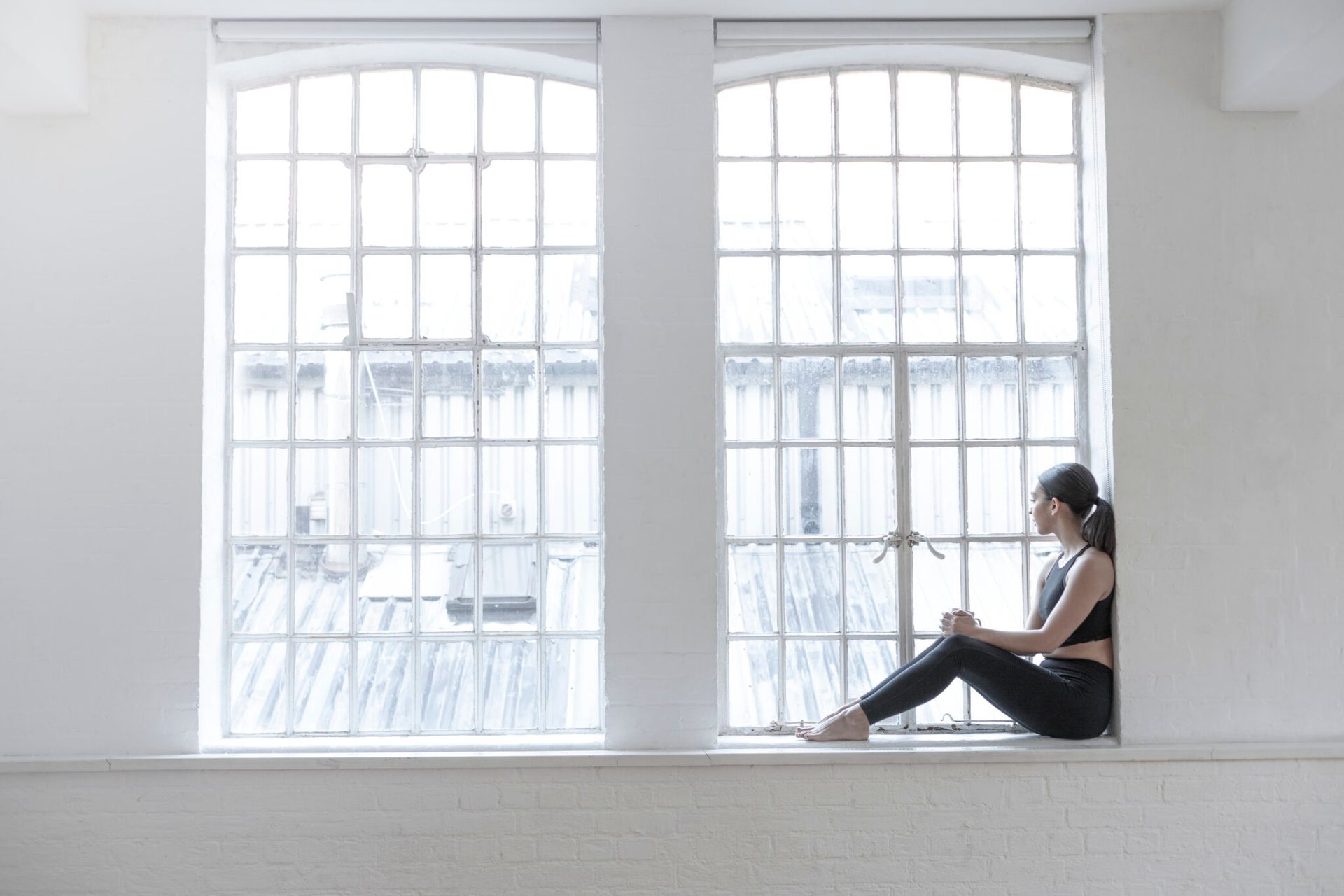 A woman is sitting on a window sill looking out the window.