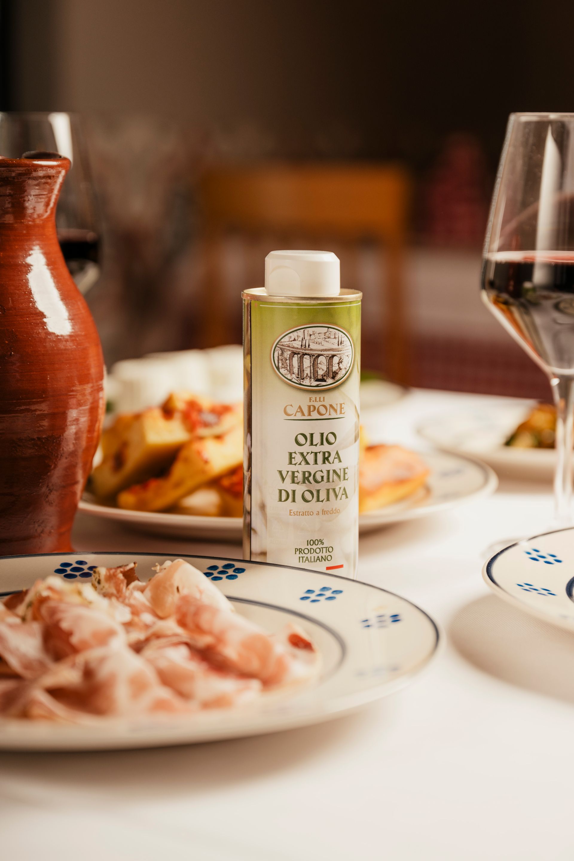 Una bottiglia di olio d'oliva è appoggiata su un tavolo, accanto a un piatto di cibo e a un bicchiere di vino.