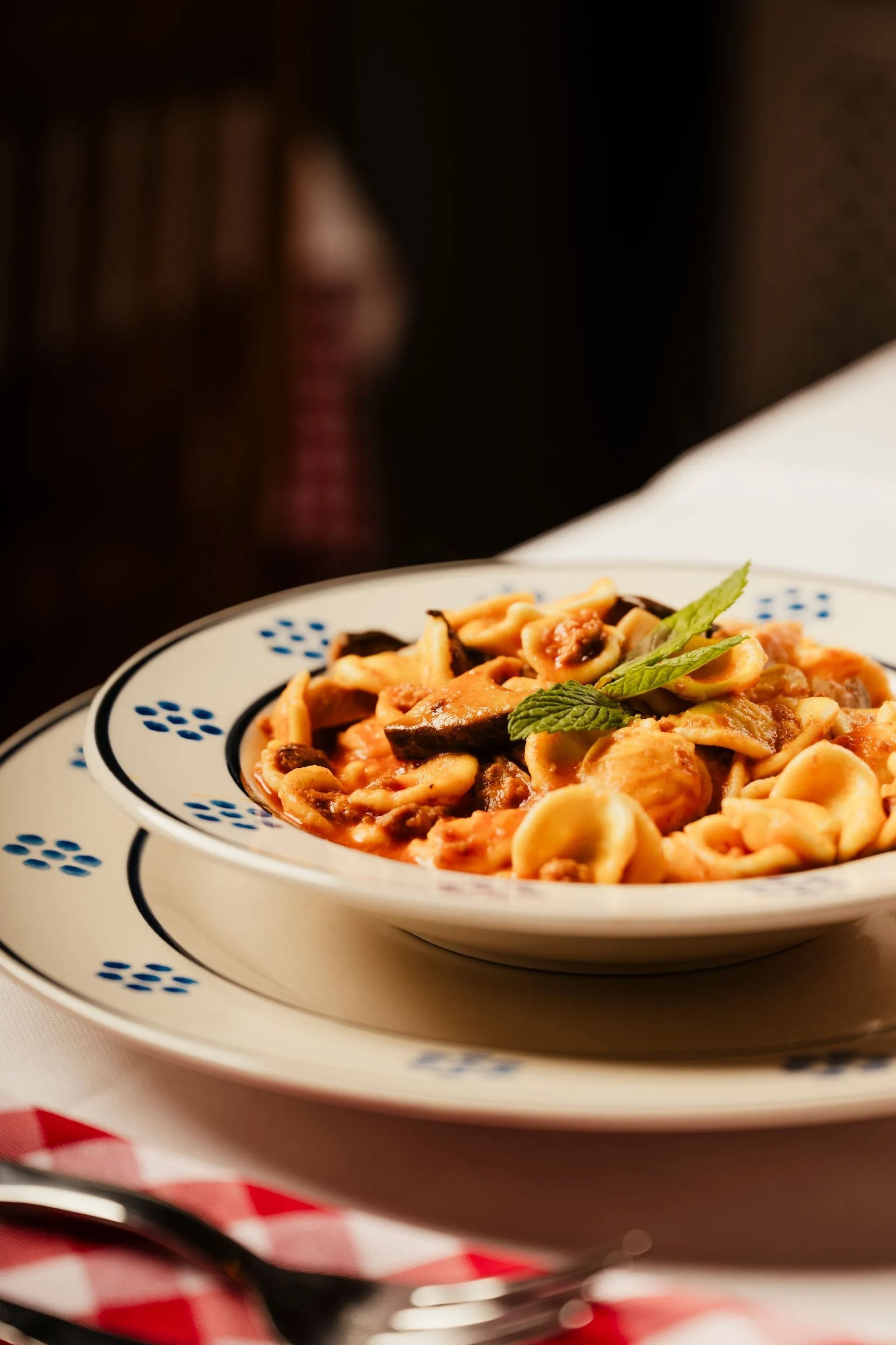 Pasta in tomato sauce topped with basil on a white plate at a restaurant table