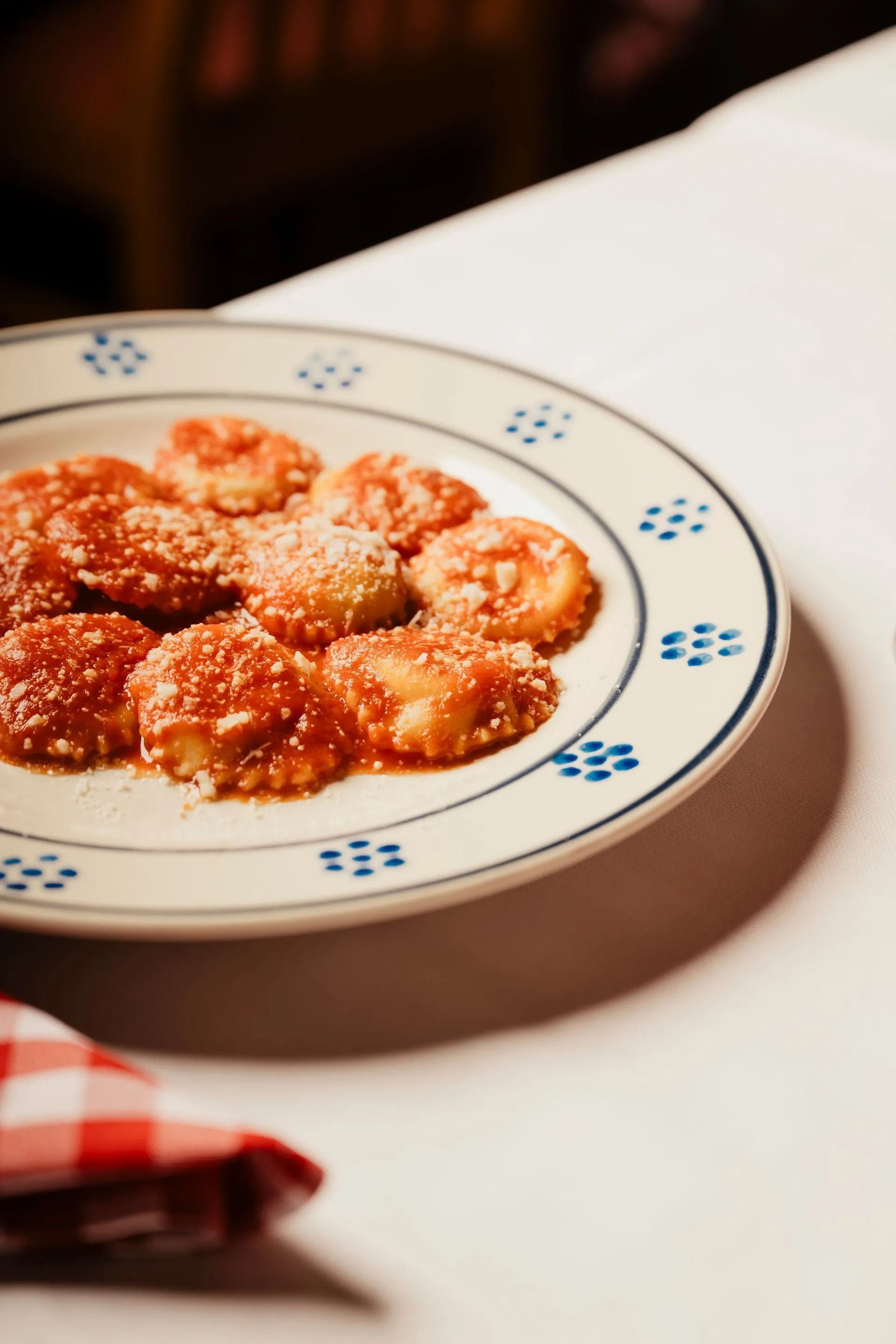 Plate of ravioli in red sauce on a white table, with a red checkered cloth nearby