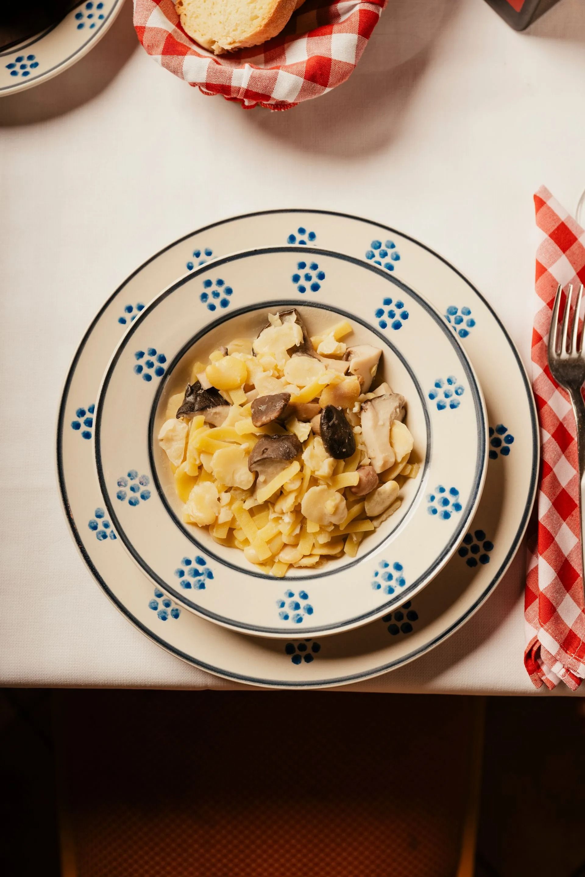 Pasta dish on a blue-floral plate on a checkered tablecloth, with bread and utensils nearby