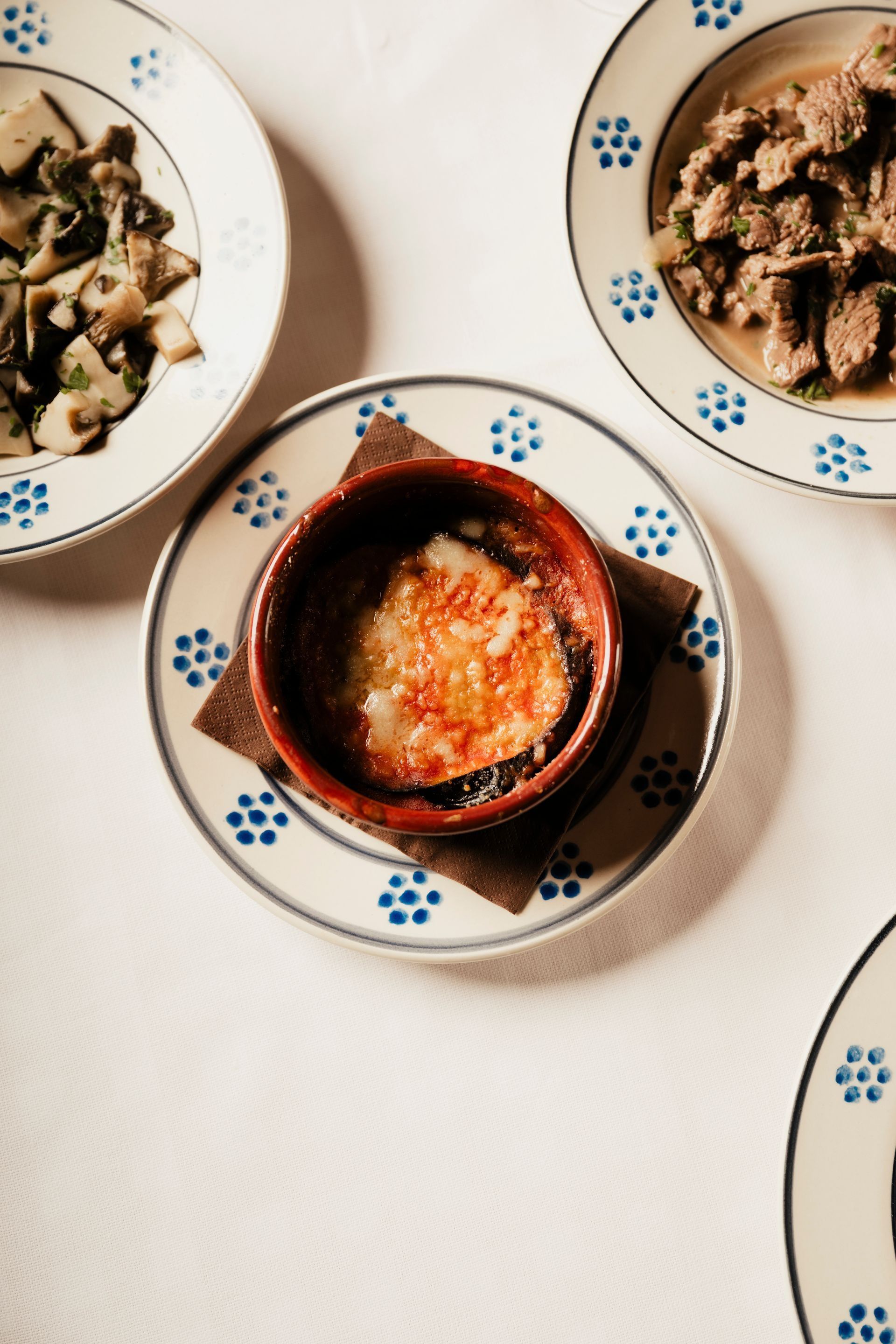 Overhead view of three dishes on patterned plates, including a central red stew in a black bowl