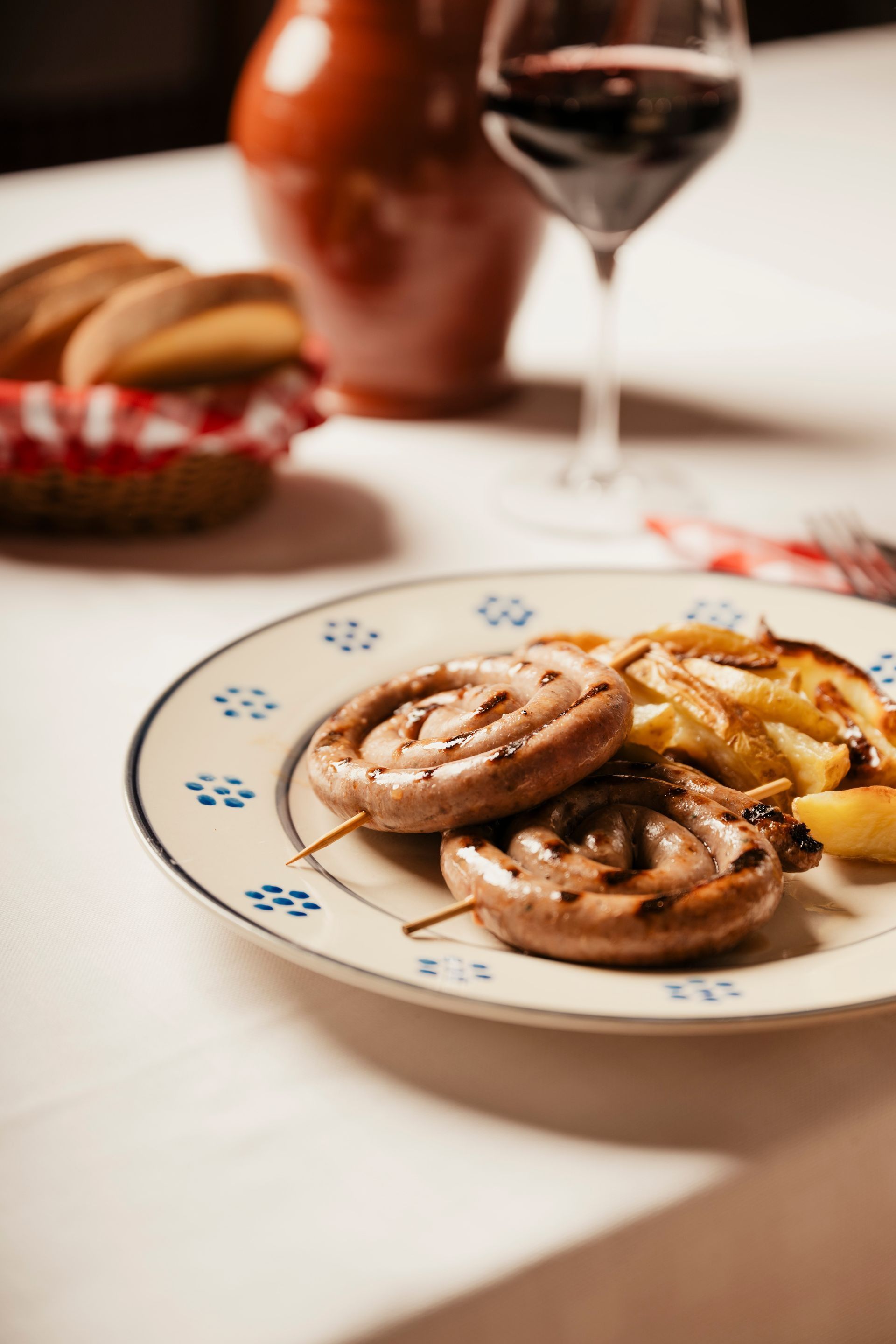 Plate of grilled mushrooms and fries on a table with wine glasses and bread in the background