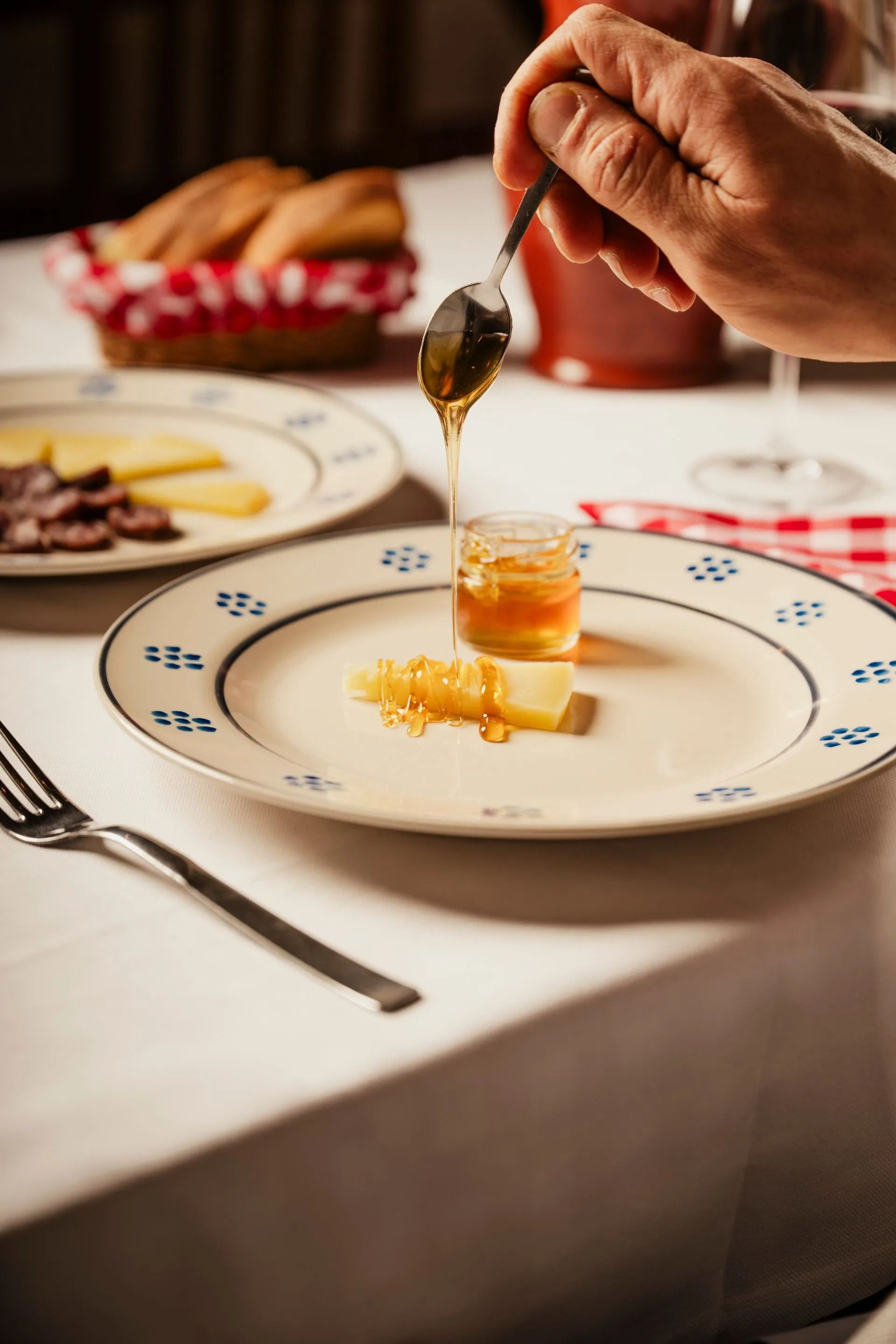Hand drizzling honey onto a small dessert on a white plate at a set dining table