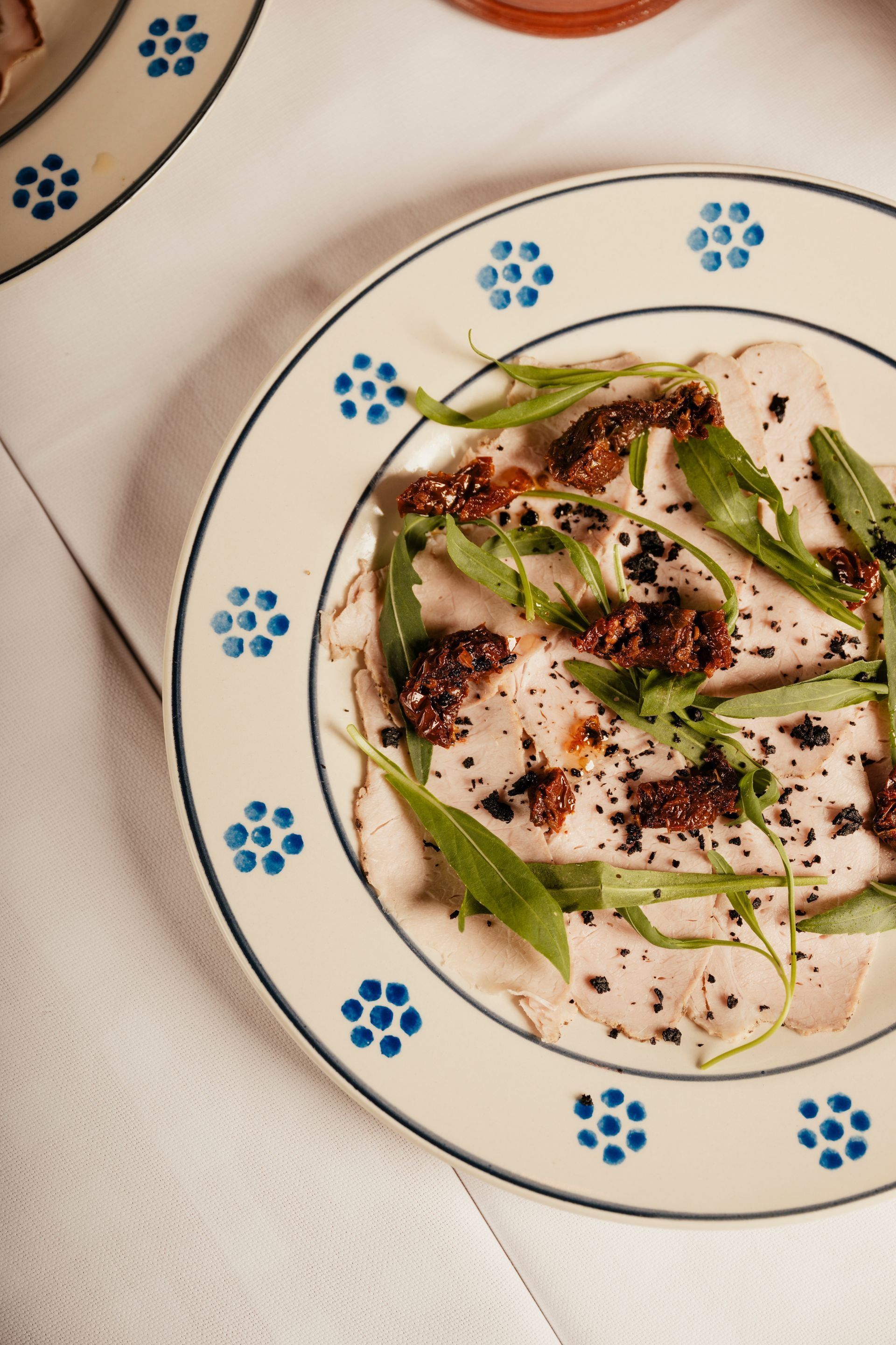 Plated gourmet dish with greens, creamy sauce, and dark crumbles on a white plate with blue floral rim