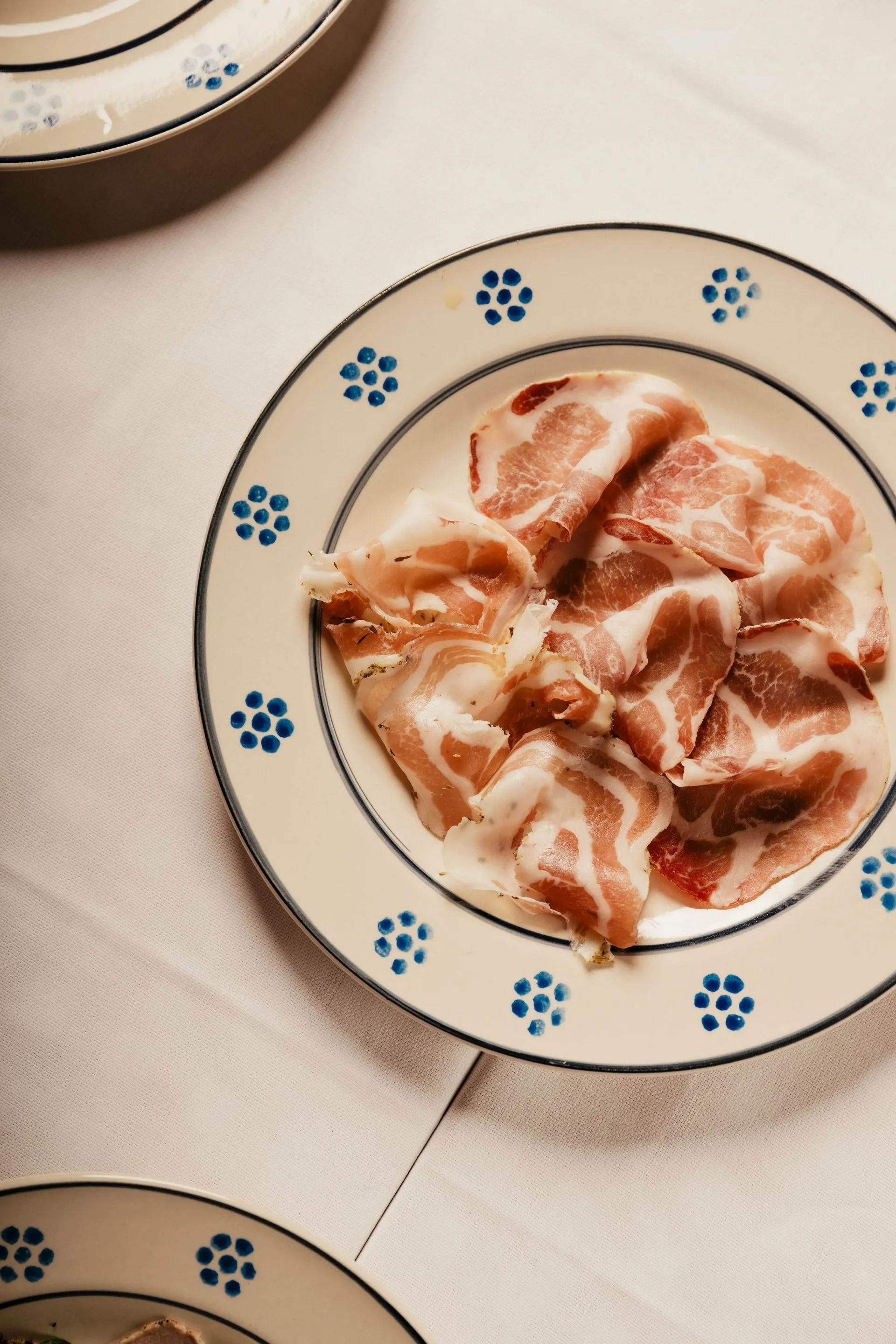 Bowl of sliced ham or prosciutto in a creamy sauce on a patterned plate